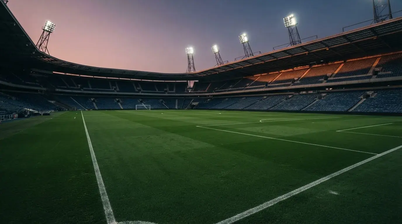 An empty football stadium with floodlight masts at dusk