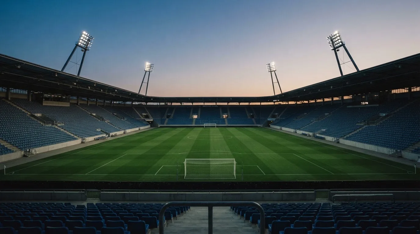 An empty football stadium with floodlight masts at dusk