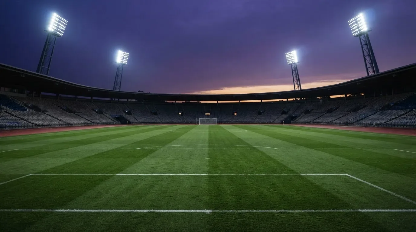 An empty football stadium with floodlight masts at dusk